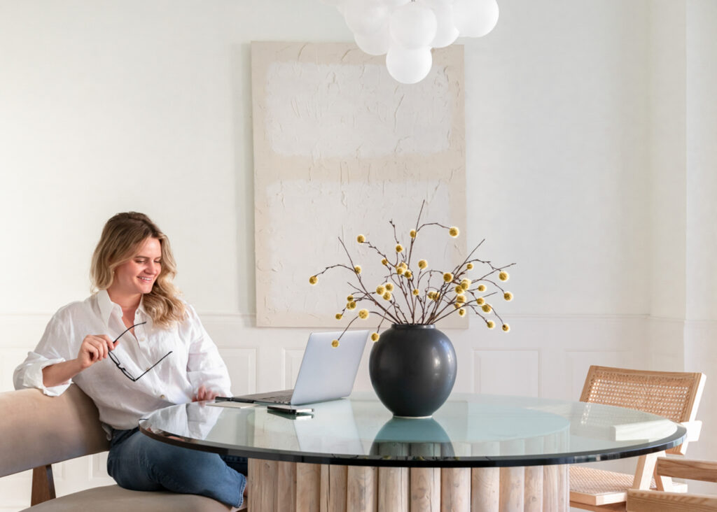 A female business owner sits at a table with a silver laptop working on her business.